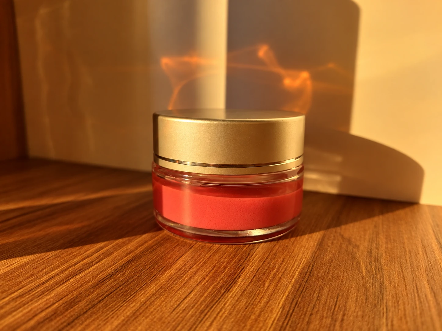 Pot de cosmétique rouge au couvercle doré, photographié dans une lumière chaude